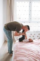 Happy father young man and baby girl little daughter having fun on bed in room at home photo