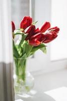 hermoso ramo de tulipanes rojos en jarrón om alféizar de la ventana en el hogar, fondo natural foto