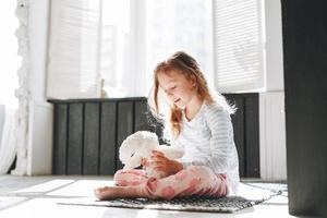 Cute little girl sitting on floor with toy at bright bath room at home photo