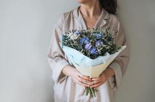 Woman in home clothes with bouqet of blue and lilac flowers in hands on grey background photo