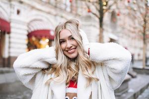 Young happy woman with blonde curly hair having fun at the Christmas fair in winter street decorated with lights photo