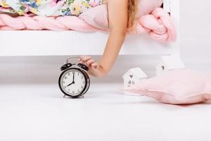 cute little hand girl reaching to turn off alarm clock on the bed in the morning, sleep and resting concept photo