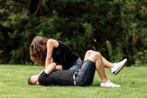 la pareja joven se divierte y juega en el césped el día de verano. mujer acostada sobre su amante, sonriendo foto