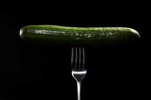 close up of fresh green cucumber on metal fork isolated on black background. Domestic cultivation. Fresh vegetables. Vegetarian dinner. photo