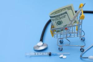 Shopping cart with pills, thermometer on a blue background. pharmacy shopping concept. buying a thermometer photo