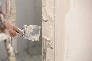 Builder using a trowel to add plaster. Plastering wall with putty-knife, close up image. Fixing wall surface and preparation for painting. construction work during quarantine photo