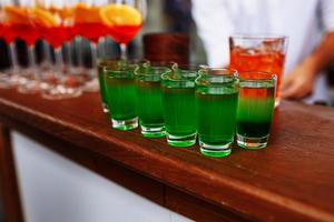 Drinks for St. Patrick's Day party. Good luck leprechaun shot cocktail. Green strong drink in a shot glass. Glasses of Aperol Spritz and Shots or Shooters on wooden bar counter in a restaurant, pub. photo