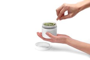 female hands are holding a white jar and using a natural green face cream or mask isolated on white background. The concept of the use of cosmetics for the body and moisture. Facial care. photo