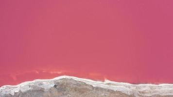 Flying over a pink salt lake. Salt production facilities saline evaporation pond fields in the salty lake. Dunaliella salina impart a red, pink water in mineral lake with dry cristallized salty coast. photo