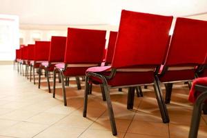 A row of upholstered red textile seats indoors. Chairs for seating the audience at the conference photo