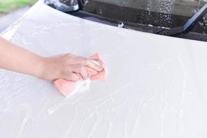 man washing a soapy white car with a pink sponge photo