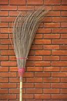 Straw broom against the orange brick wall photo