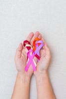 día mundial del cáncer, 4 de febrero. mano con cintas de color burdeos, naranja, rosa, melocotón y púrpura para apoyar a las personas que viven y están enfermas. concepto médico y de salud foto