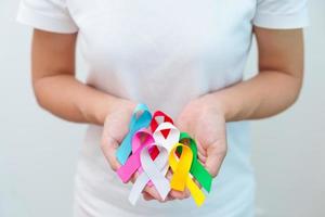 World cancer day, February 4. Hand holding blue, red, green, white, pink, grey and yellow ribbons for supporting people living and illness. Healthcare and Autism awareness day concept photo