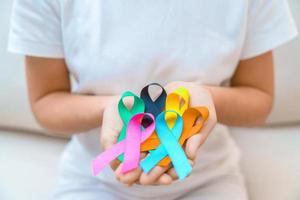 día mundial contra el cáncer, 4 de febrero. mano con cintas azules, naranjas, verde azulado, rosas, negras y amarillas para apoyar a las personas que viven y están enfermas. concepto del día de la concienciación sobre la salud y el autismo foto