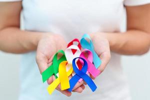 día mundial del cáncer, 4 de febrero. mano con cintas azules, rojas, verdes, blancas, rosas, azul marino y amarillas para apoyar a las personas que viven y están enfermas. concepto del día de la concienciación sobre la salud y el autismo foto