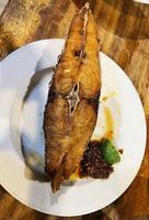 Delicious fried Spanish mackerel fish with spicy sauce and citrus served on white plate photo