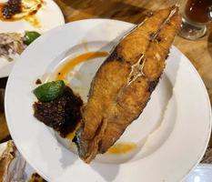 Delicious fried Spanish mackerel fish with spicy sauce and citrus served on white plate photo