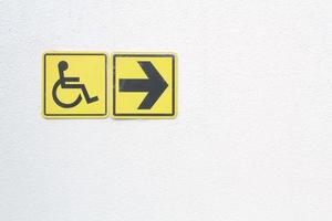 Yellow disabled sign and arrow right pointing sign on white background. Handicapped accessible sign of wheelchair. Concept of comfortable pathway for people barrier-free urban environment in city. photo