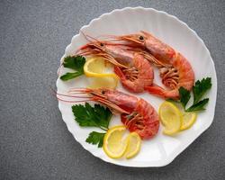 Shrimp on a white plate with lemon and parsley leaves. On a gray stone table photo