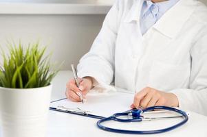 Front view at unrecognizable doctor using calculator with laptop and stethoscope near. Medical insurance concept photo