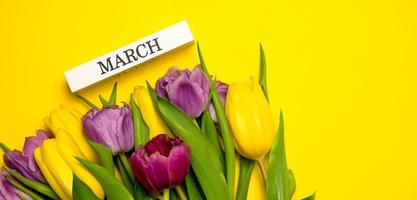 Spring banner. A bunch of yellow,pink and purple tulips and march written on a wooden block. Women's day concept photo