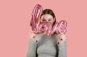 joven mujer feliz escondida detrás del amor globo. Retrato de estudio de san valentín. foto