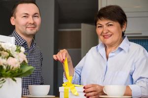 concepto del día de la madre o del 8 de marzo. anciana desempacando el regalo que su hijo le dio foto