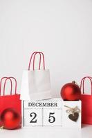 Vertical banner Colorful gift bags near wooden calendar with december 25 date and some ornaments. Advent calendar,shopping,sale photo