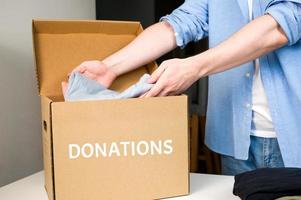 Male Volunteer puts clothes into donation box. Cardboard box with clothes for charity. Help poor.Sharity social activity. photo