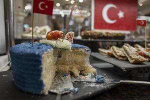 Half eaten layered cake with fruit slices and blue whipped cream on table photo