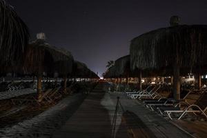 Empty boardwalk amidst deckchairs and thatched umbrellas arranged at beach photo