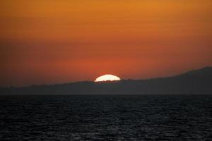 vista tranquila del hermoso paisaje marino y la puesta de sol detrás de la montaña silueta foto