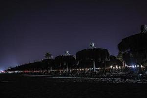 tumbonas vacías y sombrillas de paja dispuestas en la playa por la noche foto