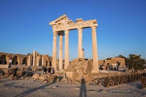 Tourists exploring old ruins of the Temple of Apollo at coastline at dusk photo