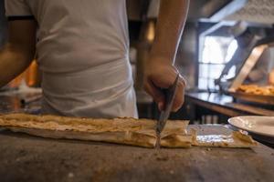 Chef cutting Turkish cheese pide into slices on table at restaurant photo