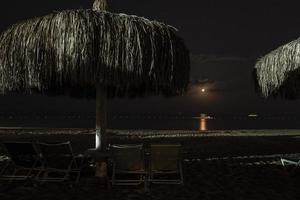 tumbonas vacías y sombrillas de paja dispuestas en la playa de arena por la noche foto