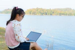 niña con laptop sentada en la orilla del río foto