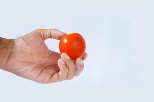 mano de un hombre asiático sosteniendo un tomate rojo solanum lycopersicum syn. Lycopersicum esculentum aislado sobre fondo blanco. foto