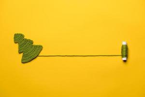 Knitted Christmas tree - a symbol of the New Year, with a spool of thread, with a place for text, on a yellow background. Copy space. photo