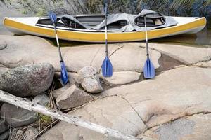 kayak para tres personas con remos estacionado en la orilla rocosa del lago, en un día de verano. descanso activo. foto