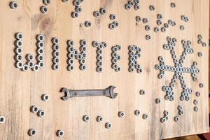 Word winter and a snowflake are lined with metal nuts on a wooden table, next to a wrench. New Year and Christmas holiday wait concept. photo