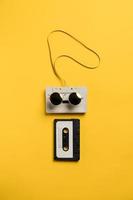 Old audio cassettes with magnetic tape, one of them wearing sunglasses, looks like a face. Yellow background. Musical concept. photo