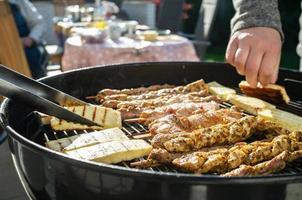 Hot grill cheese is turned over with tongs, next to it lies meat on sticks on the grate. Cooking food on the barbecue, outdoor. photo