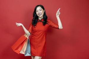 mujer china asiática con cheongsam rojo o qipao sosteniendo una bolsa de compras desea la buena suerte venta y prosperidad en las vacaciones de celebración del año nuevo chino aisladas en el concepto de fondo rojo foto