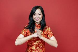 mujer china asiática con cheongsam rojo o qipao haciendo un gesto educado y respetuoso por desear buena suerte y prosperidad en la celebración del año nuevo chino aislada en el concepto de fondo rojo foto