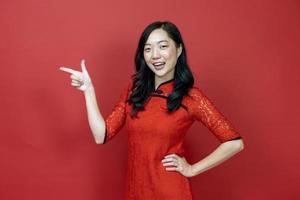 Asian woman with red cheongsam or qipao pointing to present for Chinese New Year celebration holiday isolated on red background concept photo