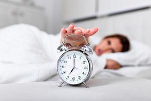 Woman lying in bed turning off an alarm clock in the morning at 7am. Hand turns off the alarm clock waking up at morning, girl turns off the alarm clock waking up in the morning from a call.