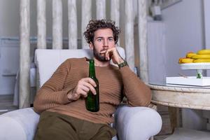 Sad sports fan sitting in an sofa and watching a match on television with his team losing the game . man watching football or soccer game on tv at home and drinking beer photo