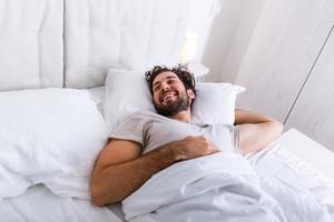 joven durmiendo despertándose y estirándose en su cama. gente, hora de acostarse y concepto de descanso - hombre acostado en la cama en casa, es hora de despertar foto